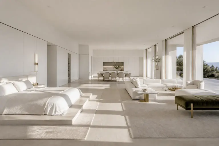 Large minimalist white open-plan bedroom suite with platform bed, sitting area, dining table and kitchen